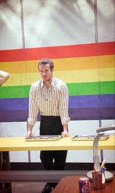 a man standing at a table in front of a rainbow wall with his hands on the tablet