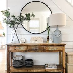 a wooden table topped with a round mirror next to a lamp and a vase filled with flowers