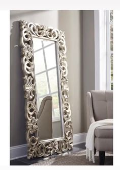 a large silver mirror sitting on top of a floor next to a chair and ottoman