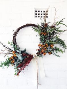 a wreath with flowers and greenery hanging on a brick wall