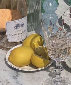 two lemons on a plate next to a bottle of wine and a glass filled with water