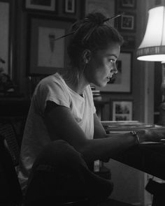 a woman sitting at a table with a laptop in front of her and a lamp on the wall behind her