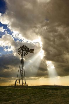 a windmill in the middle of a field with sunbeams and clouds behind it