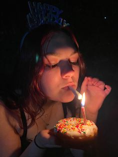 a woman blowing out a candle on a cake with sprinkles in her mouth