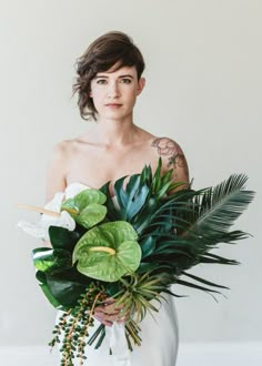 a woman in a white dress holding a large bouquet of flowers and greenery with her hands on her hips