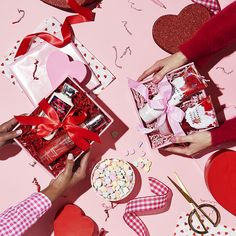 two people holding valentine's day gifts on a pink surface with hearts and ribbons