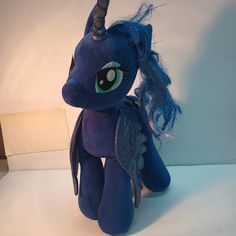 a stuffed pony with blue hair sitting on top of a white table next to a wall