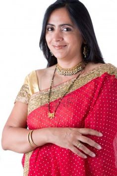 a woman in a red and gold sari with her arms crossed, smiling at the camera