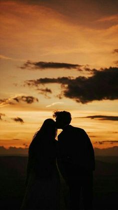 the silhouette of two people kissing in front of an orange and black sky at sunset