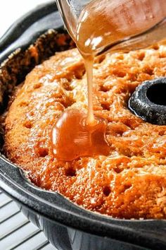 someone pouring caramel sauce on top of a baked cake in a pan with cooling rack