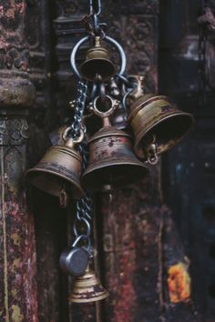 three bells hanging from chains in front of a wall with other metal objects on it