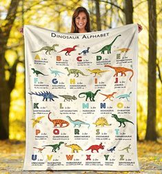 a woman holding up a blanket with dinosaur alphabets on it in the woods and trees