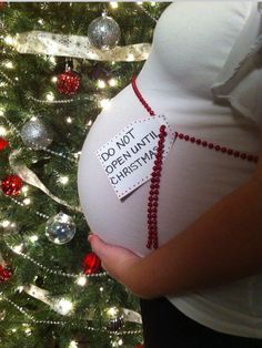 a pregnant woman holding her belly in front of a christmas tree with ornaments on it