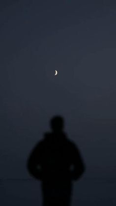 a man standing in the dark with his hands on his hips looking at the moon