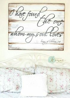 a white bed topped with pillows and a wooden sign above it's headboard