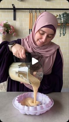 a woman pouring something into a bowl on top of a table