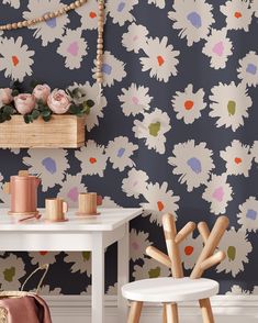 a white table and chair in front of a wall with flowers on the wall behind it