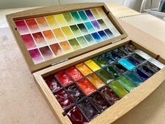 an open wooden box filled with lots of different colored paints on top of a table