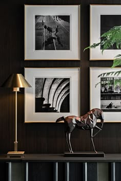 three framed photographs hang on the wall above a table with a horse statue and lamp