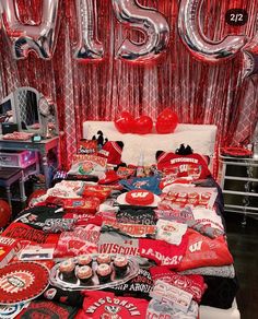 a bed topped with lots of red and silver balloons next to a table filled with cupcakes