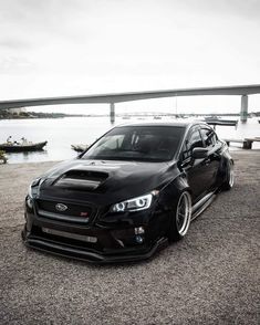 a black subarunt parked in front of a body of water with a bridge in the background