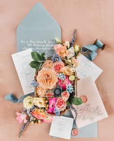 an assortment of flowers and cards on a pink surface with envelopes, ribbons and tags