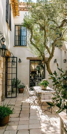 an outdoor patio with tables and chairs under a tree in front of a white building