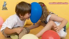 two children are sitting on the floor with balloons in front of them and one is kissing the other