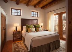 a large bed in a bedroom next to two windows and a wooden ceiling with exposed beams