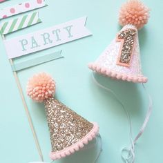 two pink and gold party hats with pom poms on them, one is for the first birthday girl