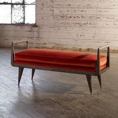 a red bench sitting on top of a hard wood floor next to a brick wall