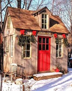 a small wooden building with red doors and wreaths on the windows in the snow