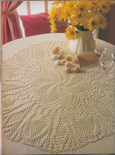 a crocheted doily sits on a table with yellow flowers in a vase