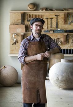 a man wearing an apron standing in front of some pottery