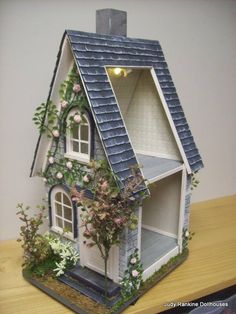 a doll house with flowers and vines on the roof is sitting on a wooden table