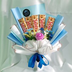 a bouquet of candy bars and flowers on a white background with blue ribbon tied around it