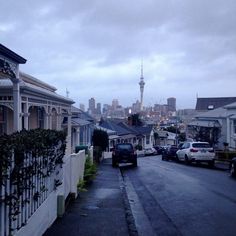 cars are parked on the street in front of some houses with a cityscape in the background