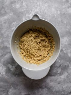 a white bowl filled with yellow powder on top of a gray countertop next to a spoon