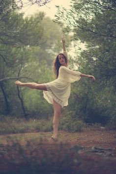 a woman is dancing in the woods with her arms spread out and legs bent forward