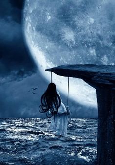 a woman standing in the ocean holding an umbrella over her head and looking at the moon