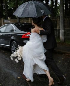 a bride and groom are walking in the rain with an umbrella over their heads,