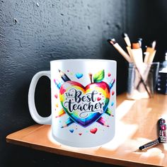 a white coffee mug with the words best teacher on it sitting on a wooden table