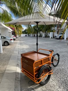 an orange bike with a cart attached to it on the side walk next to palm trees