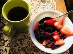 a bowl of berries and strawberries next to a cup of coffee on a doily