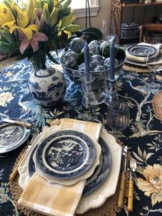 a table set with blue and white plates, silverware and flowers in vases