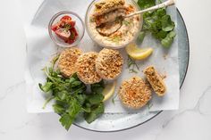 a white plate topped with food next to a bowl of dip and lemon wedges