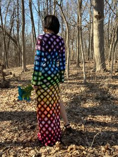 a woman standing in the woods with her back to the camera, wearing a tie dye dress