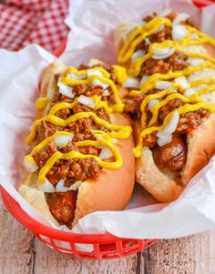 two chili dogs with cheese and onions in a red basket on top of a wooden table