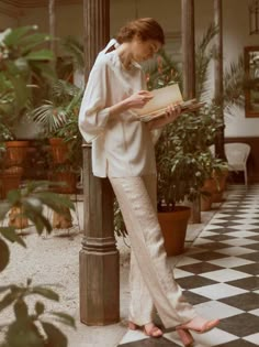 a woman in white is standing on the porch reading a book with her legs crossed