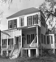 black and white photograph of an old house with porches on the second floor, stairs leading up to the second story